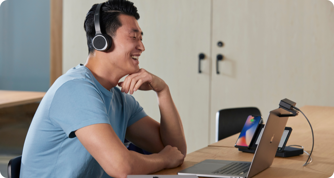 Person in a headset video conferences with colleagues on a Webex Desk Mini. Her second monitor shows a Budget Estimate slide.